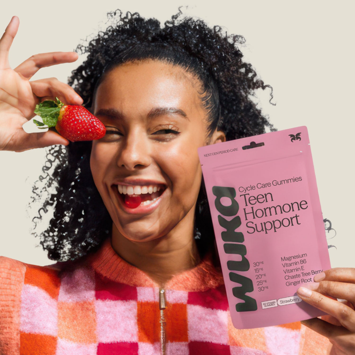 Teen girl smiling while holding WUKA Teen Hormone Support Gummies and a strawberry, promoting cycle care with natural ingredients.