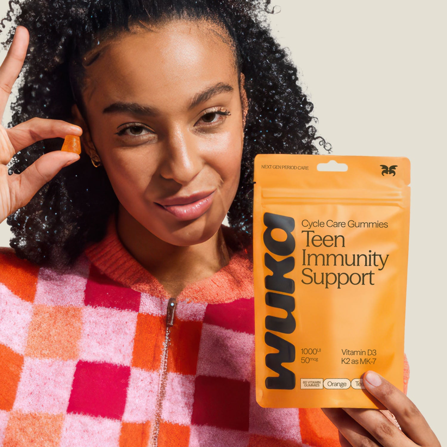 Smiling teenage girl holding WUKA teen immunity support gummies and an orange gummy, promoting daily immune support with vitamin D3 and K2.
