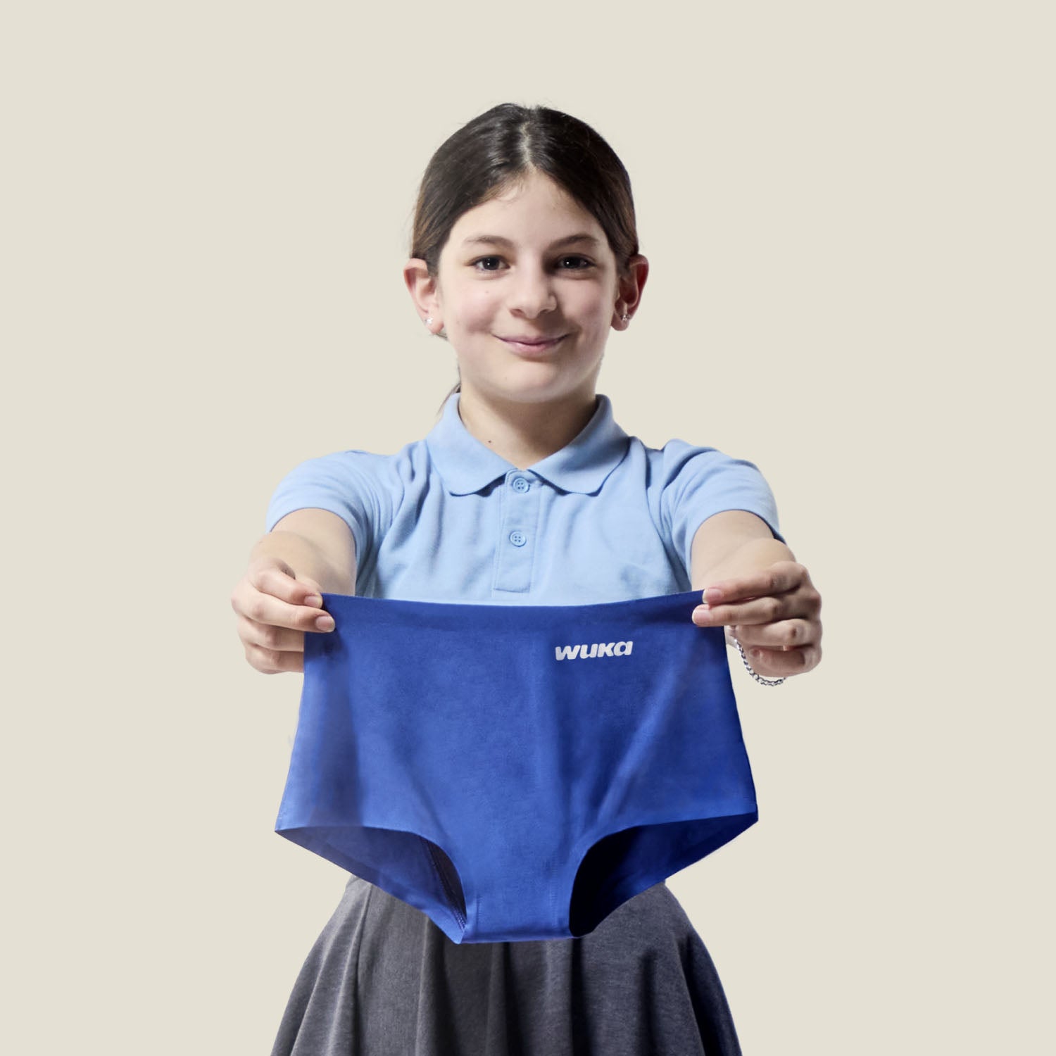 Teen girl smiling while holding a pair of blue Teen Stretch™ Boxer Shorts, showcasing their flexible fit and period-ready design.
