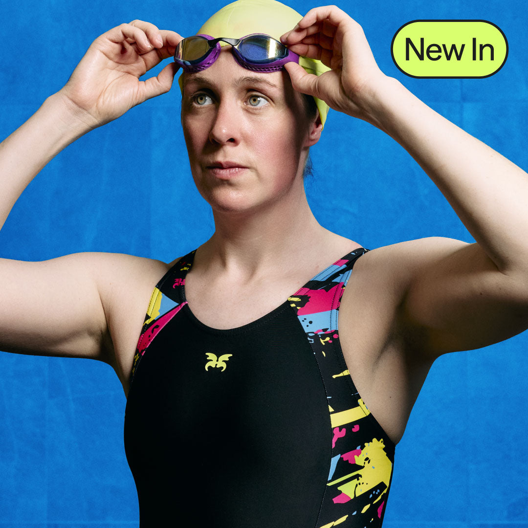 Person wearing a colourful swimsuit and swim cap against a blue background. Lunafly Competition Swimwear - heavy flow period swimwear designed to perform. Compression fit and Elite Athlete approved by Hannah Miley MBE