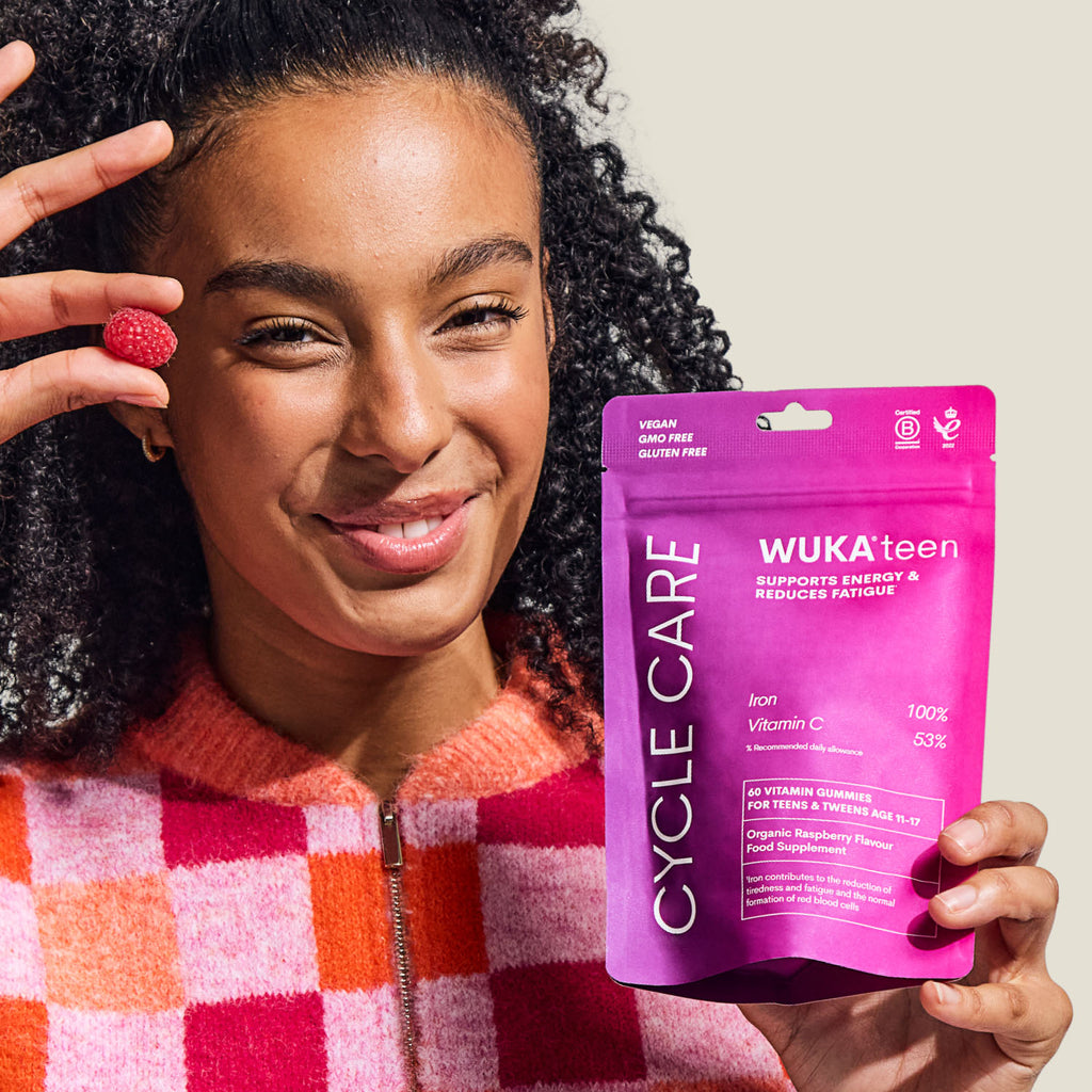 Smiling teen girl holding WUKA Teen Iron Support Gummies in raspberry flavour – vegan vitamin supplement to boost energy and reduce fatigue.