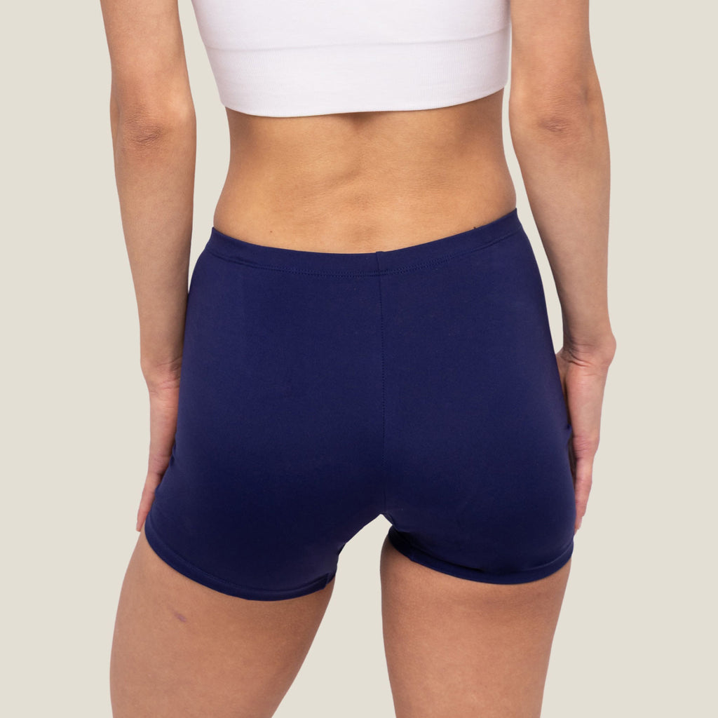 Adult female wearing swim shorts in navy blue, back view.
