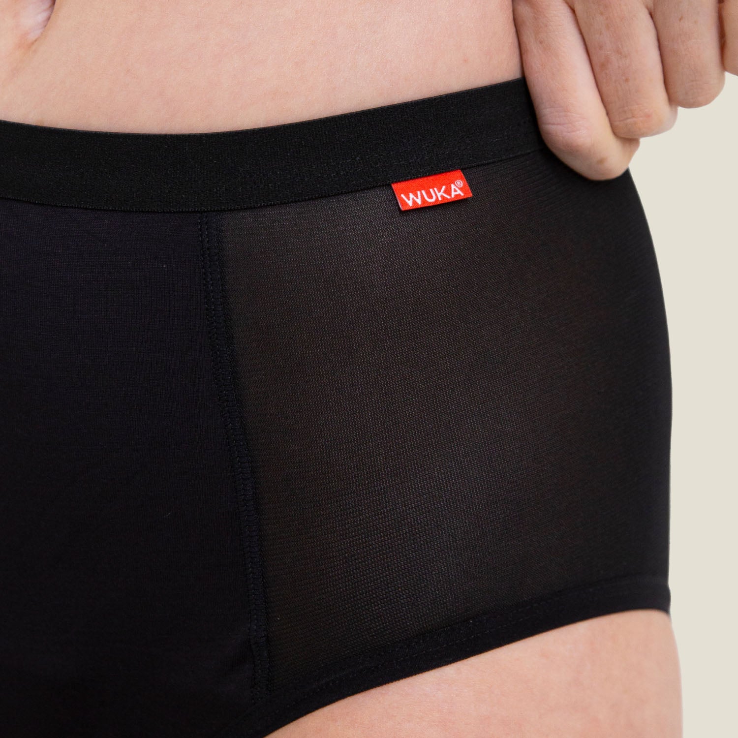 Close-up detail of WUKA Ultimate™ High Waist period pants showing the red WUKA logo and sheer mesh side panel.