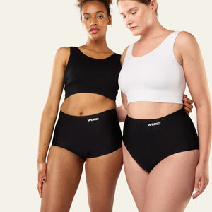 Two models wearing WUKA Stretch Boxer and High Waist period pants, one in black and one in white top, against a plain off-white background.