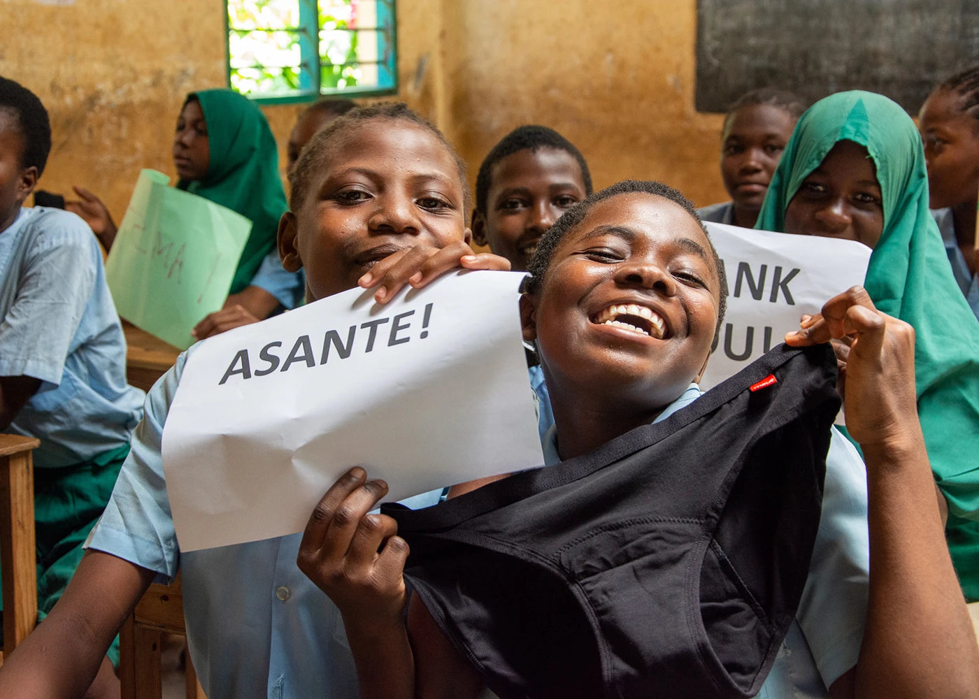 Schoolgirls smiling in classroom holding reusable period pants, highlighting impact of period poverty on education and access to sustainable period care
